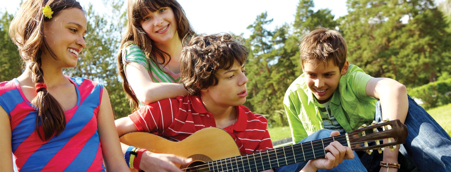 Children gathered on lawn listening to guitar being played.